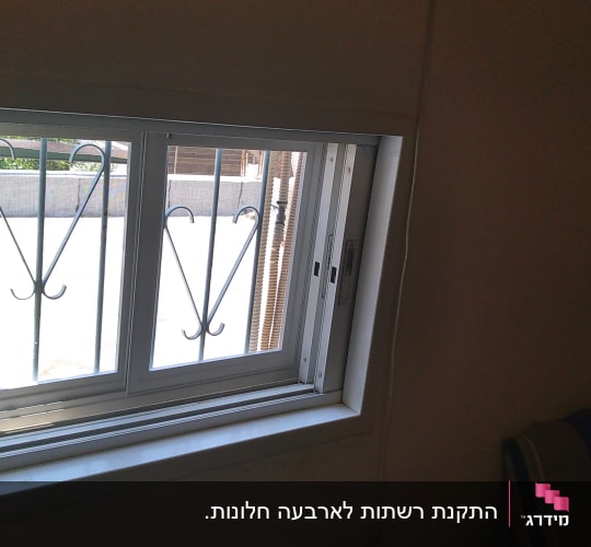 חלון הזזה מאלומיניום לבן עם רשת וסורגים בחדר